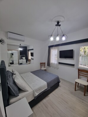 A bedroom with a bed, a desk, a chair, a TV, a mirror, and a ceiling fan. - Kardelen Otel (Bodrum)