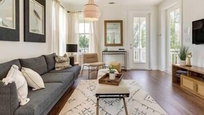A living room with a grey sofa, a coffee table, a TV, and a large window. - Pass Christian Vacation Rental < 1/2 Mi to Beach! (Pass Christian)
