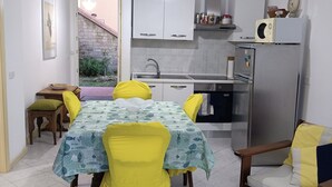 A compact kitchen with white cabinets, a stainless steel refrigerator, and a dining area with a table and chairs. - Sea view apartment (Castiglione della Pescaia)