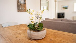 A living room with a wooden dining table, a sofa, and a potted orchid plant.