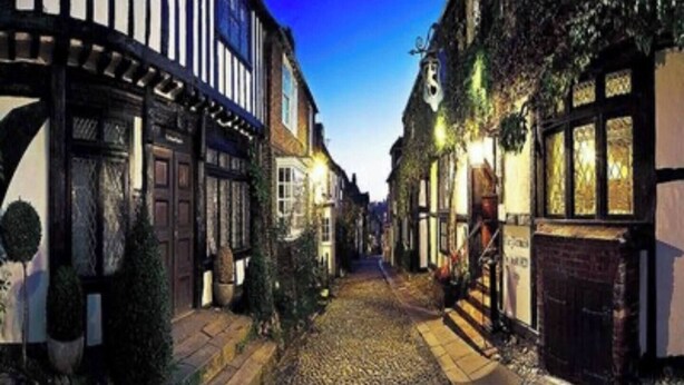 A narrow cobblestone street lined with traditional half-timbered buildings, suggesting a historic European town.