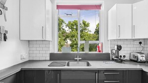 Una cocina moderna con armarios blancos, un lavamanos de acero inoxidable y una ventana con vista a árboles.