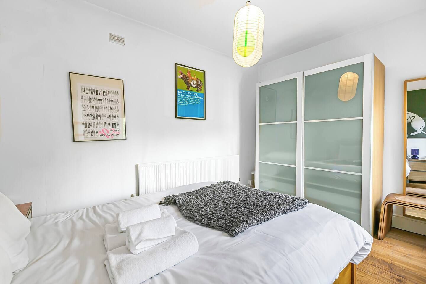A bedroom with a bed, a radiator, a wall-mounted light fixture, a framed poster, and a sliding glass door closet.