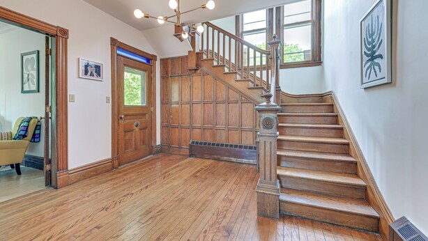 A spacious room with wooden flooring, a staircase with a wooden railing, and a large window providing natural light. - Family Home w/ Yard & Fire Pit in Middleburgh! (Middleburgh)