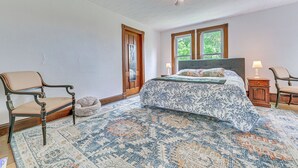 A bedroom with a large bed, two windows, a chandelier, and a patterned rug. - Family Home w/ Yard & Fire Pit in Middleburgh! (Middleburgh)