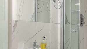 Une salle de bain avec un lavabo en marbre blanc, une douche en verre et un mur recouvert de carreaux de marbre.