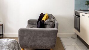 Une cuisine moderne avec un canapé gris, une petite table et un mur recouvert de carreaux.