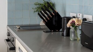 Une cuisine dotée d’un plan de travail en acier inoxydable, d’un porte-couteaux noir, d’un vase en verre contenant des fleurs et d’un grille-pain.