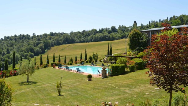 Zona de piscina con vista despejada del paisaje circundante, incluyendo un campo cubierto de césped y árboles.