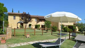 Un patio con cerca de madera, una sombrilla blanca y dos sillones de descanso.