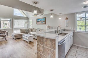 Una cocina moderna con una isla central, un rincón de comedor con sofá y mesa, y ventanas amplias que aportan luz natural.