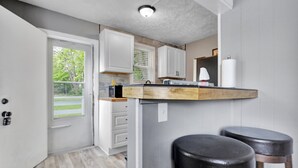 A kitchen with white cabinets, a wooden countertop, and two black stools. - Charming 1 Bedroom House in Lansing, MI (Lansing)