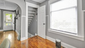 A hallway with wooden flooring, a white door, and a large window with blinds. - Charming 1 Bedroom House in Lansing, MI (Lansing)