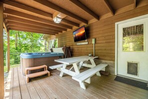 Ein ĂŒberdachter AuĂenbereich mit Whirlpool, Picknicktisch und einem an der Wand befestigten Fernseher.