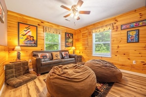 Ein gemĂŒtliches Blockhaushaus-Interieur mit einer Couch, zwei SitzsĂ€cken, einem Deckenventilator und HolzwĂ€nden.