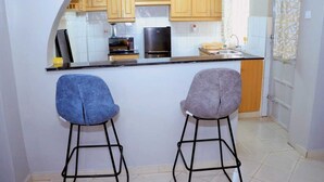 A kitchen with wooden cabinets, a black countertop, and two bar stools. - Lux Suites Okiega Apartments Kisii (Kisii)
