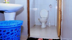 A small bathroom with a white sink, a toilet, and a blue plastic basket. - Lux Suites Okiega Apartments Kisii (Kisii)