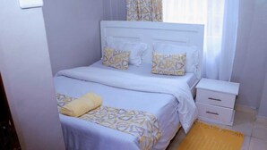 A bedroom with a bed, bedside table, and a yellow rug. - Lux Suites Okiega Apartments Kisii (Kisii)