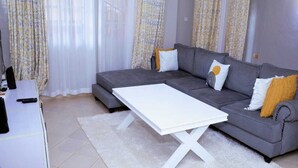 A modern living room with a grey sofa, white coffee table, and patterned curtains. - Lux Suites Okiega Apartments Kisii (Kisii)