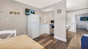 A compact kitchen with white cabinets, a refrigerator, and a microwave. There is a dining area with a wooden table and chairs. - Pelican Pointe 323:Walk to Beach~Pool~Free Parking (Clearwater Beach)