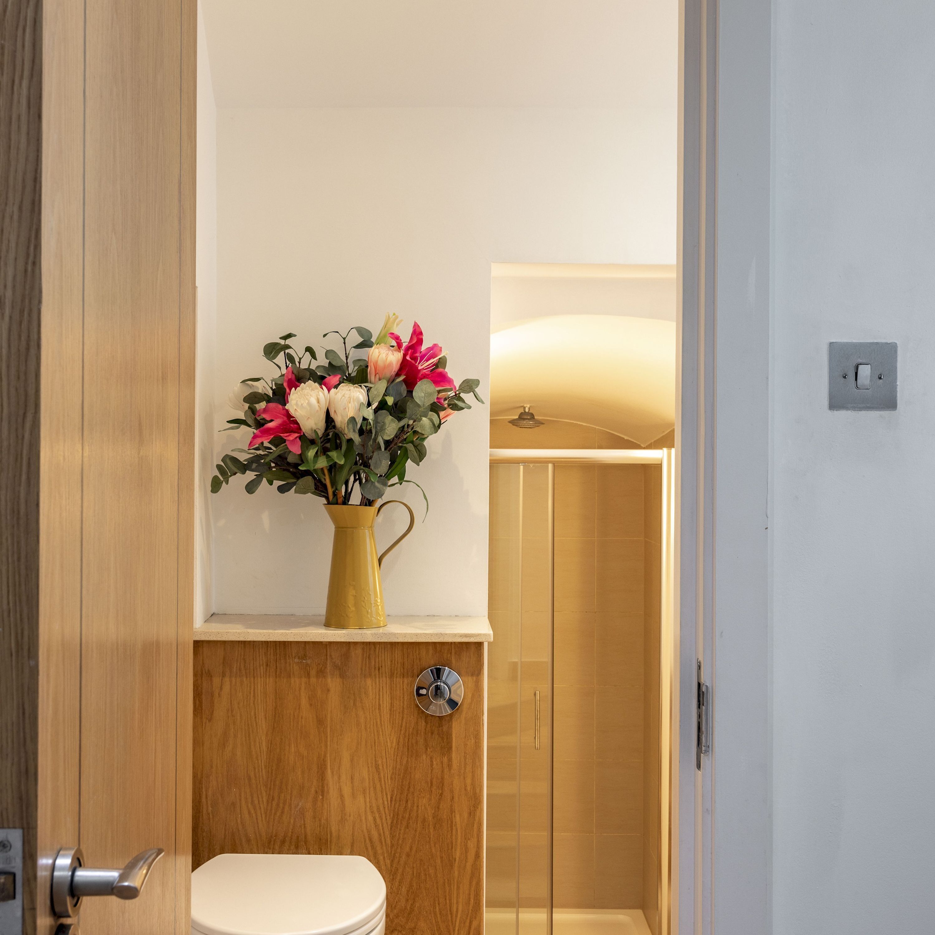 Un baño con inodoro, ducha y un florero sobre una estantería.