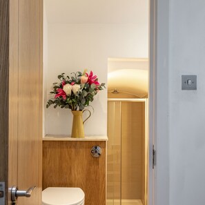 Een badkamer met toilet, douche en een bloemenvaas op een plank.