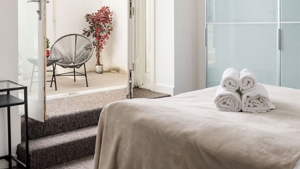 A hotel room with a bed, a chair, a potted plant, and a glass door leading to an outdoor area. - Luxury 2 Bedrooms Flat Next to Harrods (London)