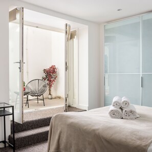 Hotelkamer met een bed, een stoel, een kamerplant en een glazen deur naar een buitenruimte.
