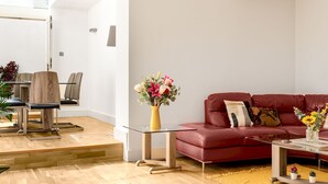 A modern living room with a red sofa, a glass coffee table, and a dining area with wooden chairs. - Luxury 2 Bedrooms Flat Next to Harrods (London)