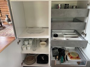 A kitchen with open cabinets displaying utensils, cookware, and a decorative plate.