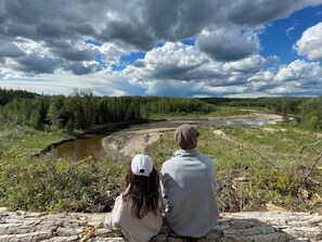 Two people sitting on a stone ledge overlooking a river and forest. - At The River — Secluded Cabin with Private River Access (Woodlands County)