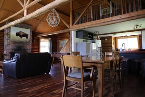 A rustic interior with a dining area, a fireplace, and a loft space.