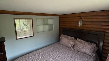 Un dormitorio con cama, un cuadro enmarcado, una ventana y una lámpara fijada a la pared.