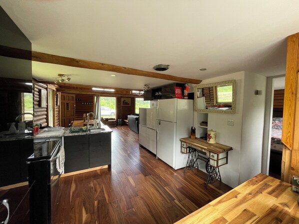 A spacious kitchen with wooden floors, a central island, and a dining area with a wooden table. - At The River — Secluded Cabin with Private River Access (Woodlands County)
