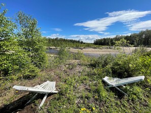 A natural landscape with a river, trees, and two wooden benches.