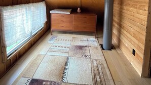 A wooden attic bedroom with a window, a radiator, a wooden dresser, and a patterned rug.