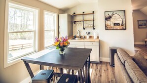 A modern kitchen with a dining area, large windows, and a farmhouse-style wall art. - Red Dog Farms Modern Studio Apt (Rocky Point)