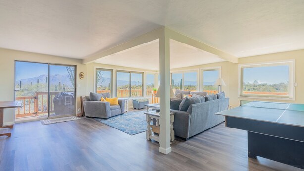 A spacious living room with a ping pong table, a sofa, and a balcony with a view of the desert. - The heart of the desert with amazing views and hiking trails right outside! (Tucson)
