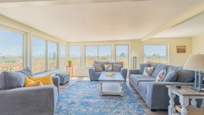 A spacious living room with two grey sofas, a coffee table, and a blue patterned rug. Large windows offer views of a desert landscape. - The heart of the desert with amazing views and hiking trails right outside! (Tucson)
