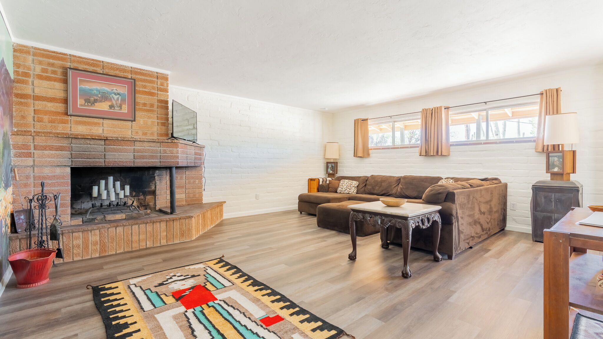 Una sala de estar con chimenea de ladrillo, un juego de sofá, una mesa de centro de madera y una alfombra estampada.