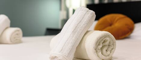 A neatly made bed with two rolled white towels and a single orange pillow.