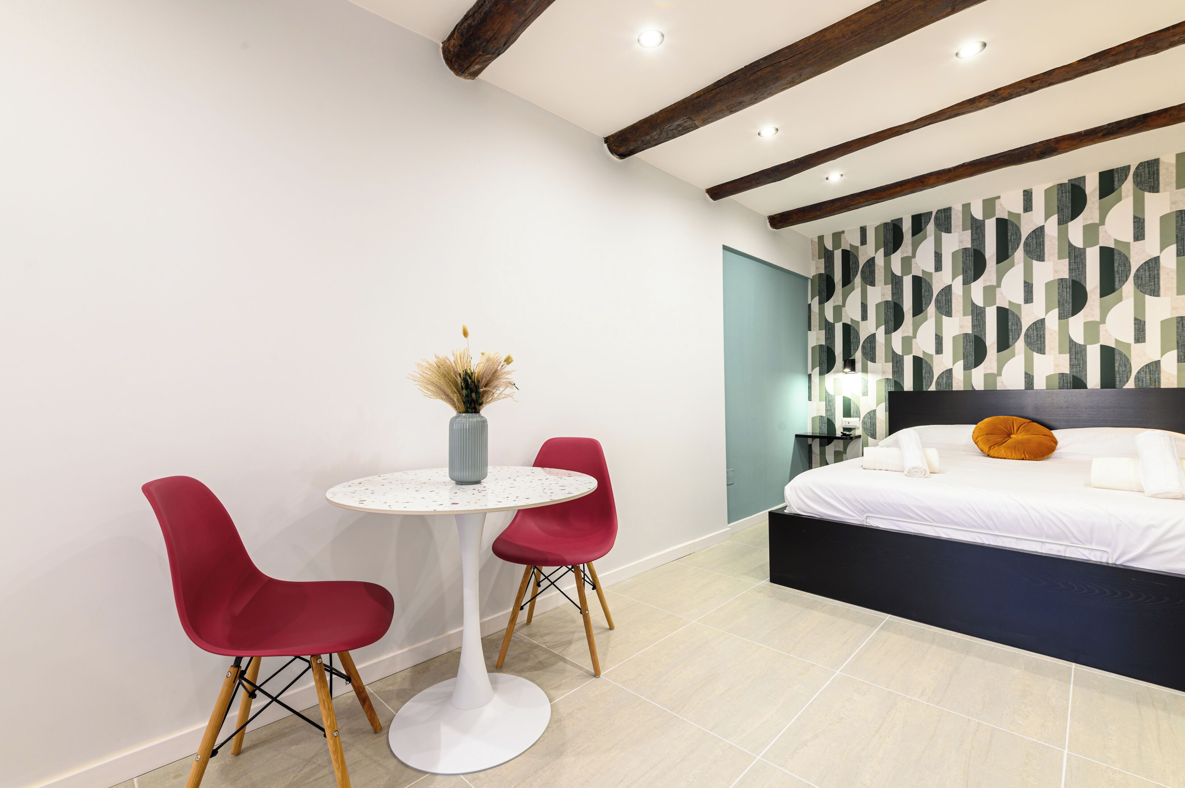 A modern bedroom with a bed, a small round table, and two red chairs.