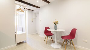 Une pièce moderne avec une table blanche et deux chaises rouges, un vase contenant des fleurs séchées et une chaise en bois avec un porte-manteau.