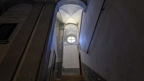 Un escalier étroit, surmonté d’une fenêtre circulaire, menant à un étage supérieur.