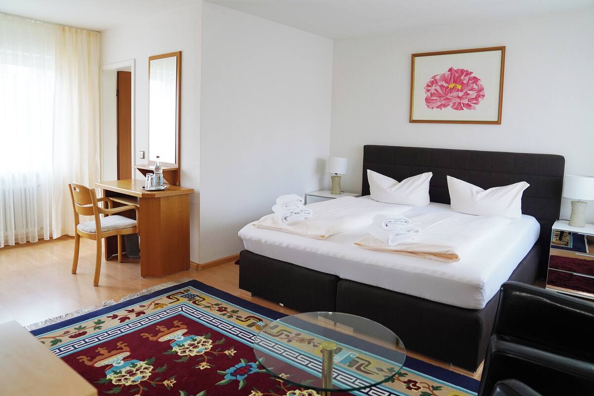 Ein Hotelzimmer mit Bett, Schreibtisch, Stuhl, Spiegel und einem gerahmten Bild an der Wand.