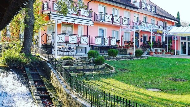 Un hotel de varios pisos con balcones, un jardín y un pequeño arroyo.