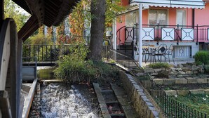 Un canal con agua corriente, rodeado de escalones de piedra y vegetación. Se observa un edificio con fachada rosa y barandillas negras.