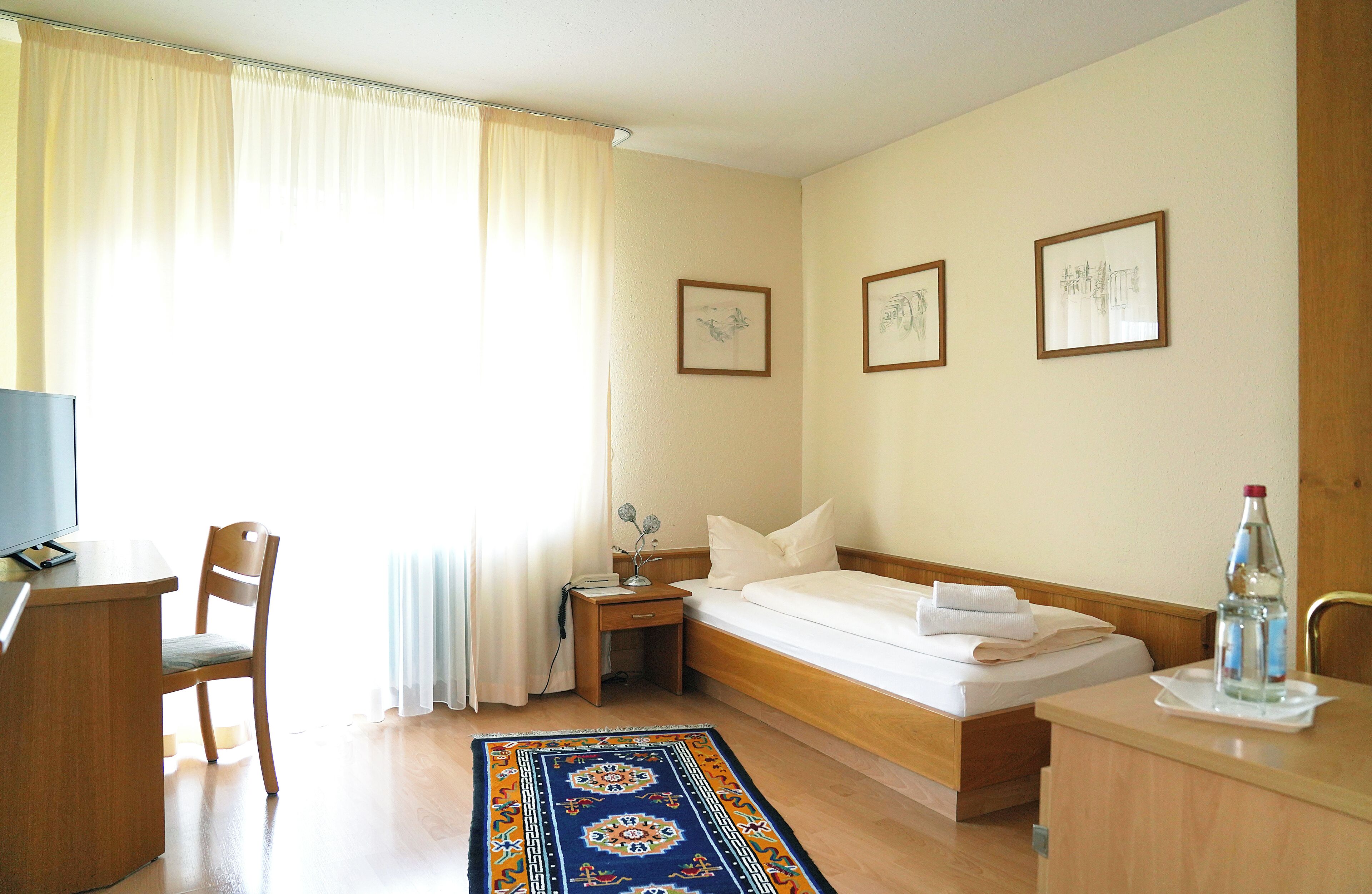 A hotel room with a bed, a desk, a chair, a nightstand, and a bedside table.