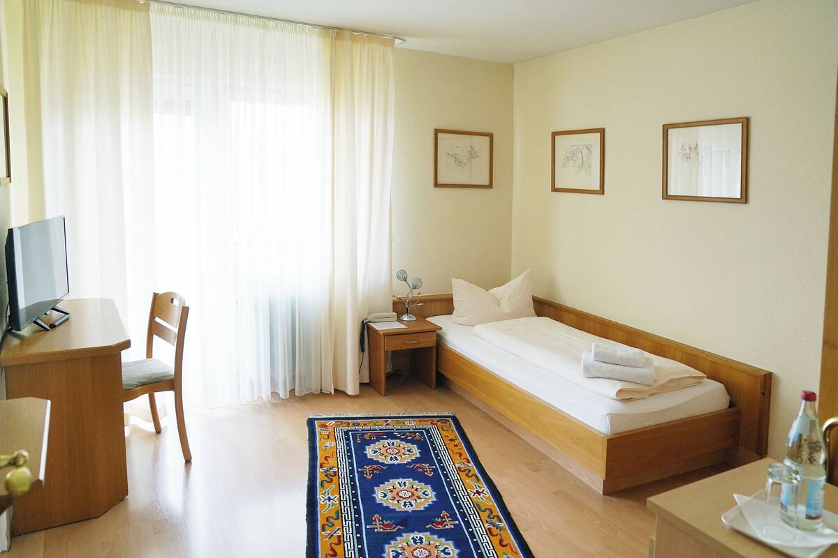 Ein Hotelzimmer mit Bett, Schreibtisch, Stuhl, Nachttisch und einem Fenster mit Vorhängen.