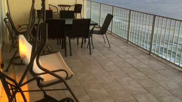 A balcony with a table and chairs, a painting on the wall, and a view of the sea.